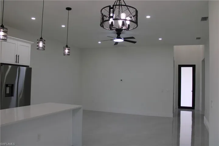 Open-concept living space featuring a kitchen island with a light-toned countertop, stainless steel refrigerator, white shaker-style cabinetry with dark hardware, a ceiling fan with integrated lighting, and recessed lighting