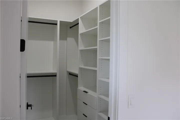 Custom white closet system featuring multiple shelves, hanging rods, and integrated drawers with black hardware