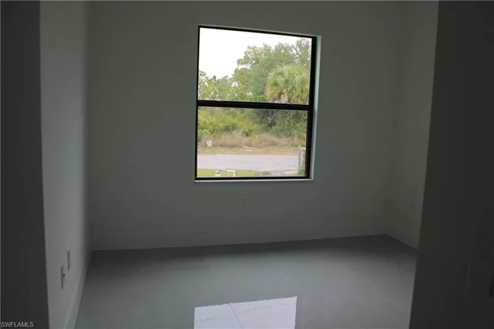 Interior room featuring light-toned wall finishes, a large window with black framing, and neutral-toned tile flooring