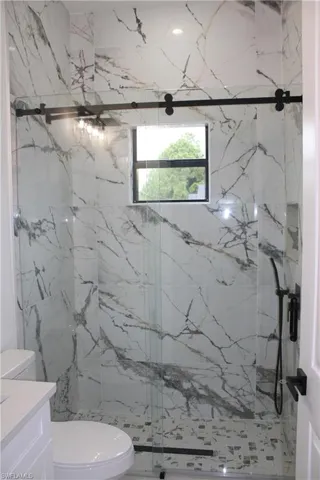 Walk-in shower featuring large format marbled tile walls, a mosaic tile floor, and a matte black sliding glass door system