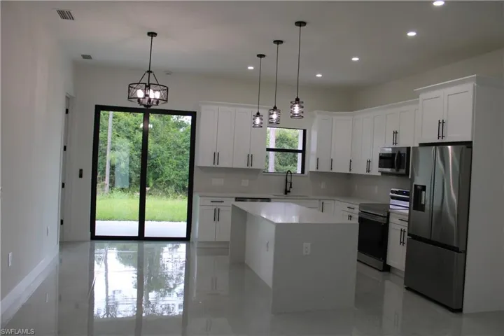 Contemporary kitchen featuring white shaker cabinetry, stainless steel appliances, a center island with a solid surface countertop, recessed lighting, and modern pendant fixtures