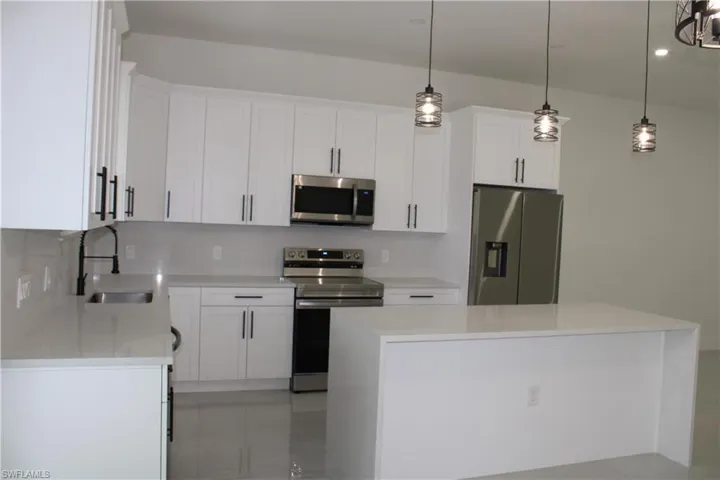 Modern kitchen featuring white shaker cabinetry with matte black hardware, stainless steel appliances, a white waterfall island, pendant lighting, and light-toned tile flooring