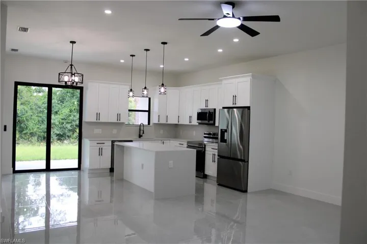 Open-concept kitchen featuring white shaker cabinetry, stainless steel appliances, a center island with a stone countertop, and glossy tile flooring