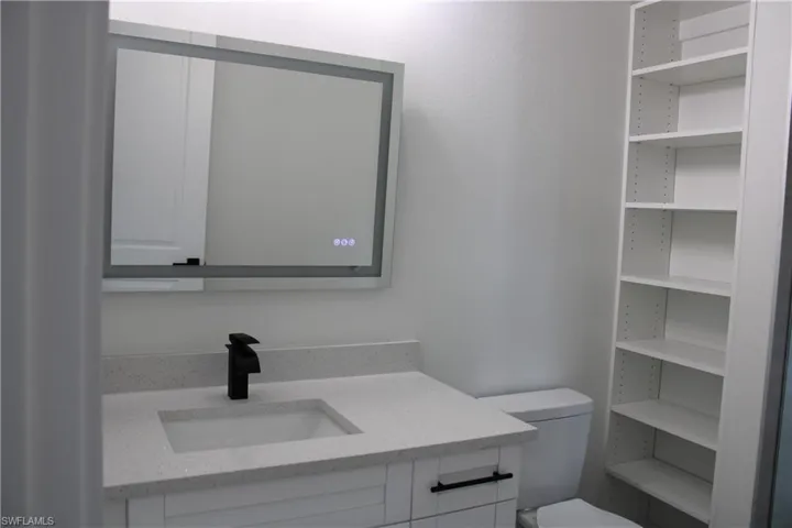 Modern bathroom vanity with a white rectangular undermount sink, speckled countertop, and matte black faucet