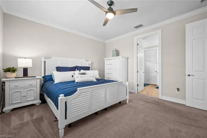 Bedroom with ceiling fan, ornamental molding, and carpet