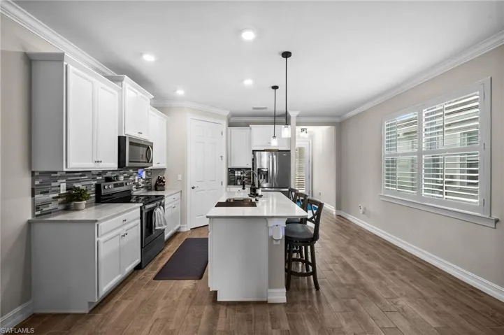 Kitchen featuring dark wood-type flooring, pendant lighting, white cabinetry, appliances with stainless steel finishes, and a center island with sink