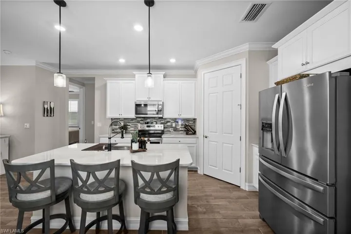 Kitchen featuring pendant lighting, an island with sink, white cabinetry, stainless steel appliances, and dark hardwood / wood-style flooring