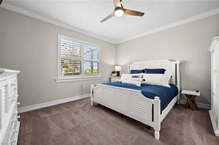 Bedroom with ornamental molding, dark colored carpet, and ceiling fan