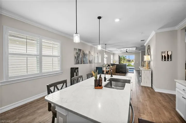 Kitchen featuring white cabinets, hanging light fixtures, ornamental molding, a center island with sink, and hardwood / wood-style flooring