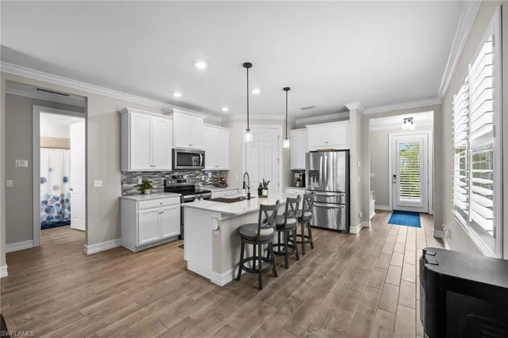 Kitchen featuring stainless steel appliances, a kitchen island with sink, light wood-type flooring, and white cabinetry