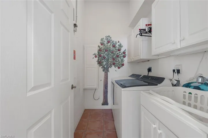 Clothes washing area with light tile patterned floors, washing machine and dryer, cabinet space, and baseboards