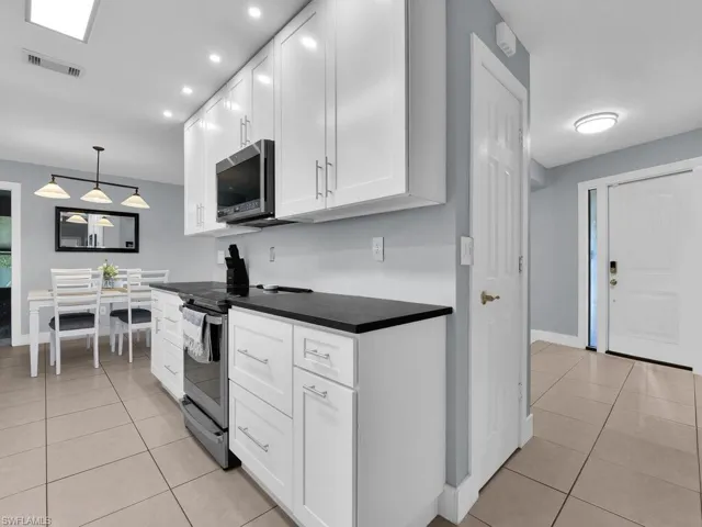 Kitchen with appliances with stainless steel finishes, dark countertops, light tile patterned flooring, white cabinets, and pendant lighting