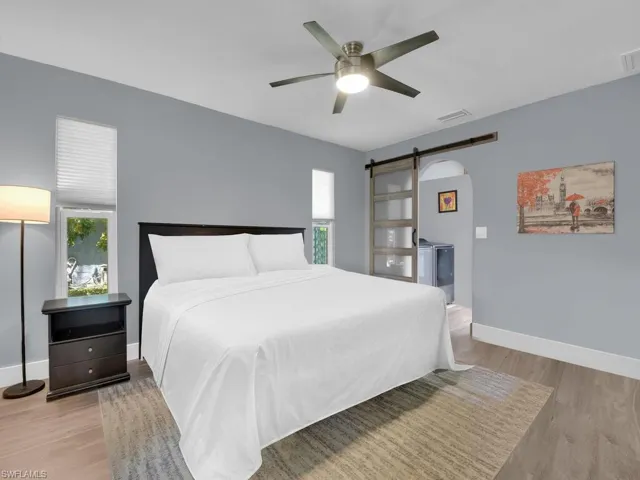 Bedroom with a barn door, wood finished floors, and ceiling fan