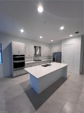 Kitchen with sink, an island with sink, fridge, double oven, and extractor fan