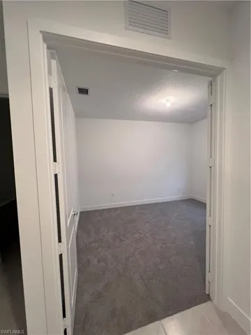 Empty room with a textured ceiling and dark colored carpet