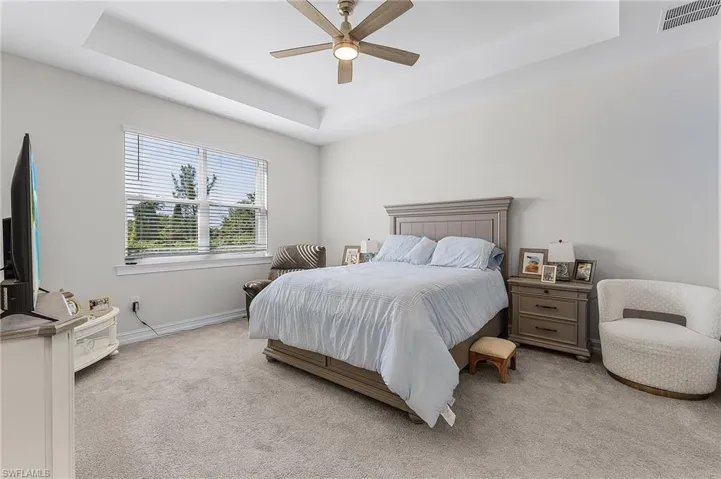 Bedroom featuring ceiling fan, light colored carpet, and a tray ceiling