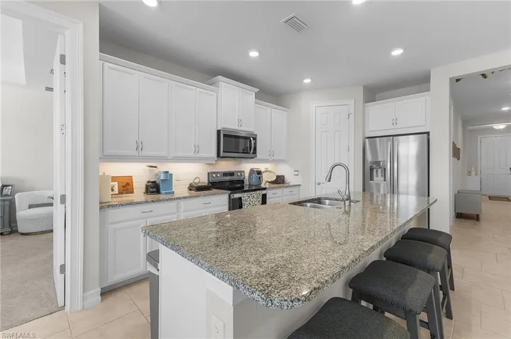 Kitchen featuring a kitchen island with sink, sink, white cabinets, and appliances with stainless steel finishes