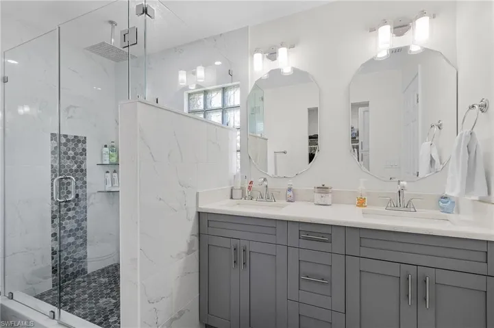 Full bathroom with double vanity, a sink, and a marble finish shower