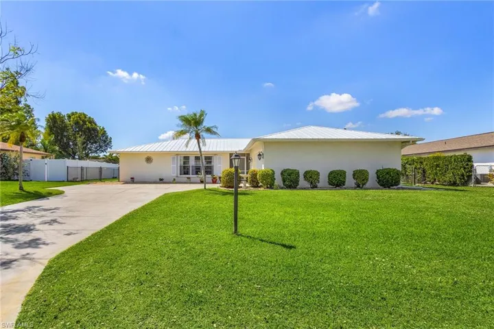 View of front of property featuring metal roof, fence, a front lawn, and stucco siding