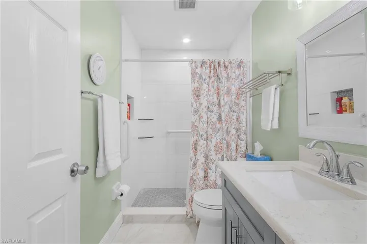 Full bath with toilet, visible vents, vanity, marble finish floor, and a tile shower