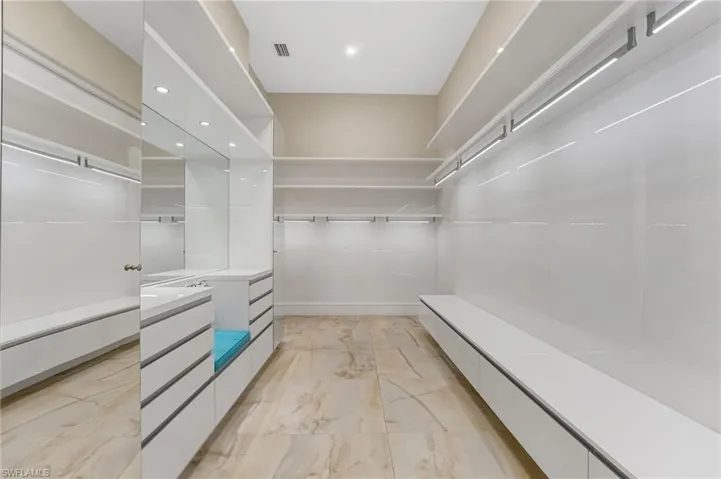 The primary closet is exceptionally spacious and thoughtfully designed, featuring custom lighting, a dedicated dressing area, bespoke built-in cabinetry, and a transom window that fills the space with beautiful natural light.