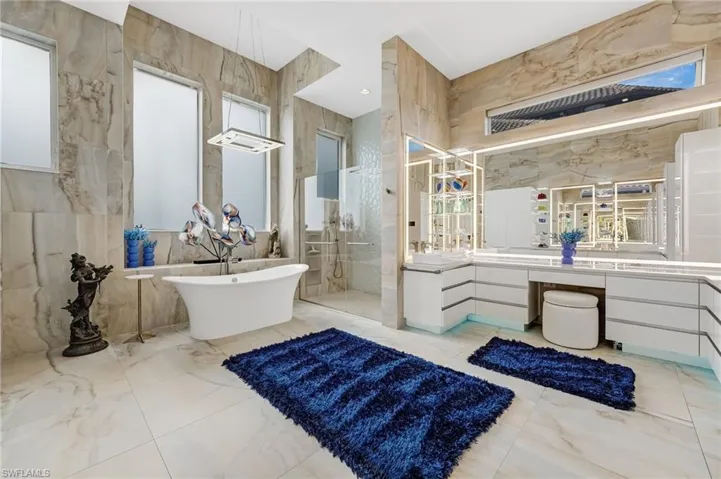 Designed as a private sanctuary, the oversized primary ensuite boasts backlit mirrors with a built-in television, a heated towel rack, porcelain-clad walls, a spacious walk-in shower, and a refined freestanding soaking tub.