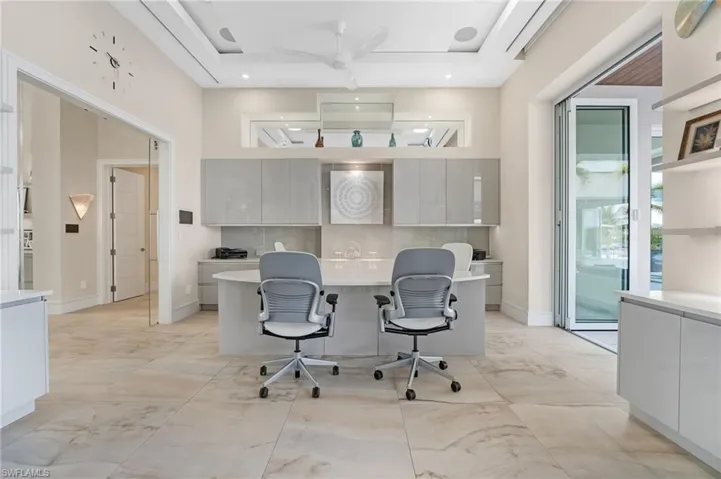 The dedicated office features a built-in desk and custom storage, maintaining a sleek and streamlined aesthetic with unobstructed views throughout the space. Thoughtfully designed, it includes seamless glass barn doors for refined privacy, while two additional walls of 12-foot accordion hurricane doors open effortlessly to the covered seating area, creating a bright, airy, and seamlessly connected workspace.
