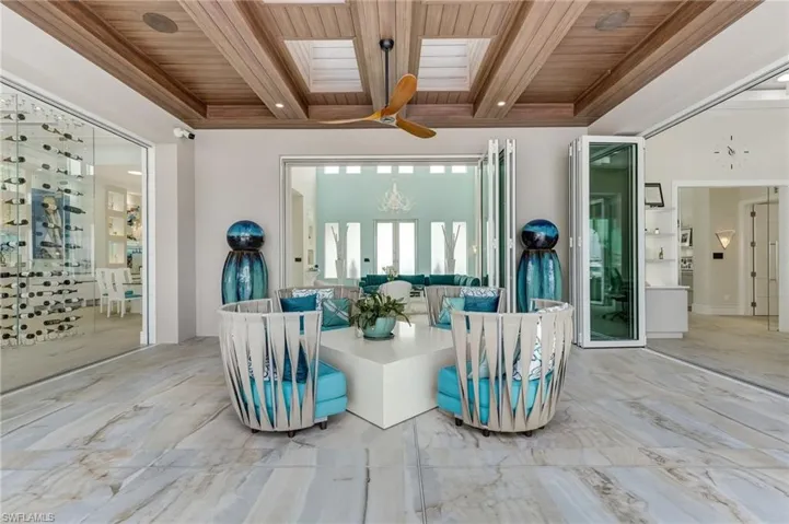This exceptional covered outdoor space is ideally positioned off the office, main living area, and kitchen—creating a seamless extension of the home from the moment you enter. A custom wood-beamed ceiling adds warmth and architectural character, while all three adjoining spaces are framed by expansive 12-foot accordion hurricane-impact doors, effortlessly blending indoor comfort with outdoor living.