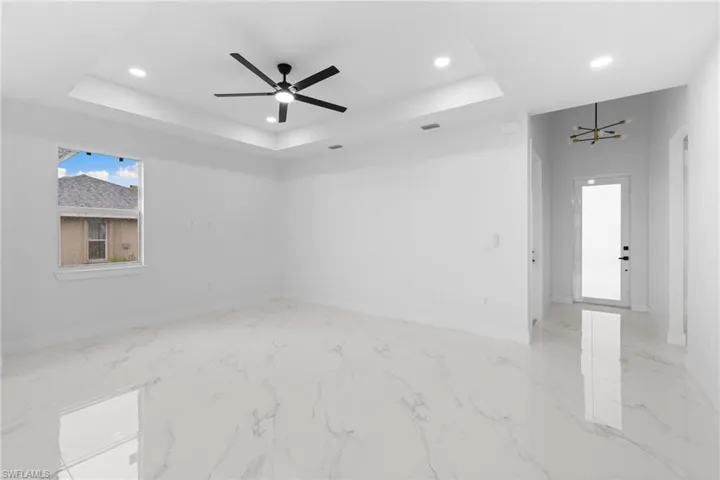 Spare room featuring a tray ceiling, recessed lighting, baseboards, a chandelier, and light marble finish floors