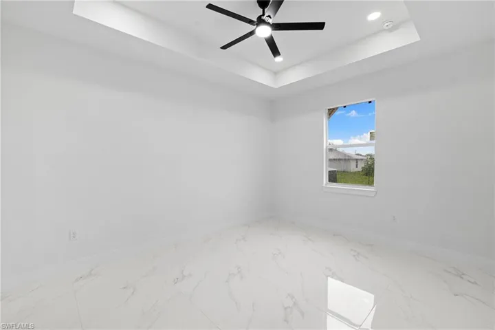 Spare room featuring baseboards, a raised ceiling, marble look tiles, and recessed lighting
