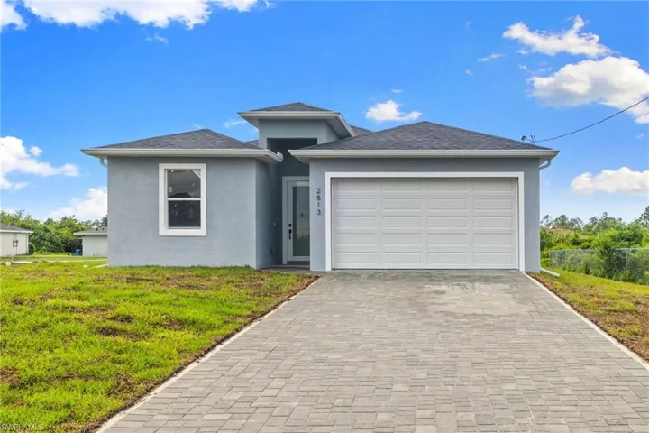 View of front of house with stucco siding, a front lawn, an attached garage, and decorative driveway
