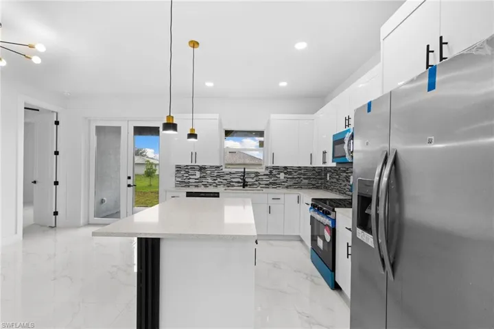 Kitchen with stainless steel appliances, a sink, light marble finish floors, a center island, and decorative backsplash