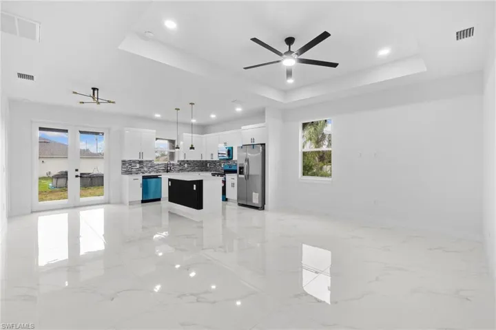 Unfurnished living room featuring light marble finish flooring, healthy amount of natural light, a tray ceiling, ceiling fan, and recessed lighting