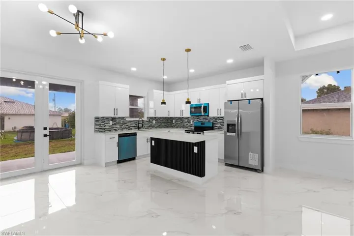 Kitchen with appliances with stainless steel finishes, a chandelier, a kitchen island, light marble finish flooring, and hanging light fixtures