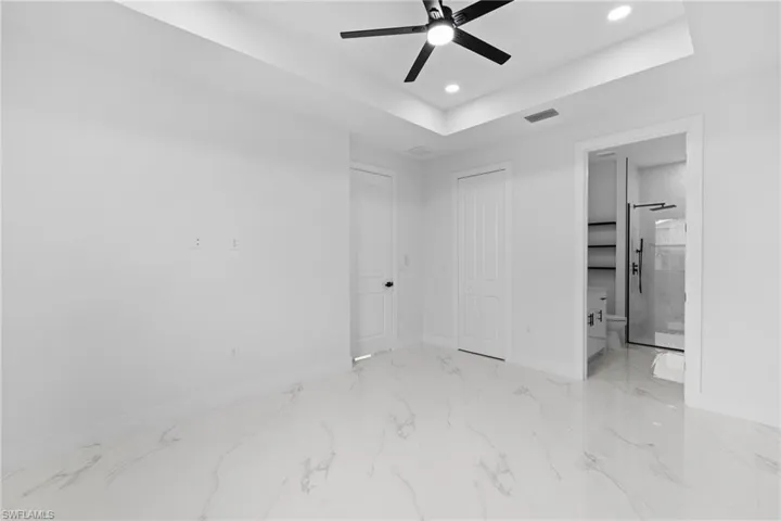 Unfurnished bedroom with recessed lighting, baseboards, marble finish flooring, a tray ceiling, and connected bathroom