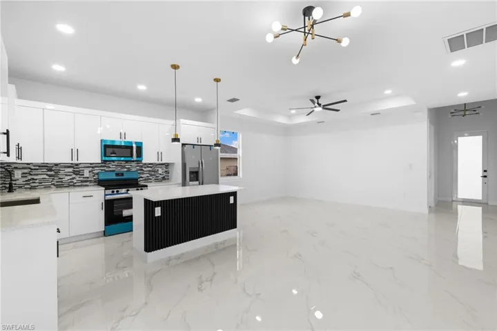 Kitchen with stainless steel appliances, a sink, recessed lighting, a raised ceiling, and a kitchen island