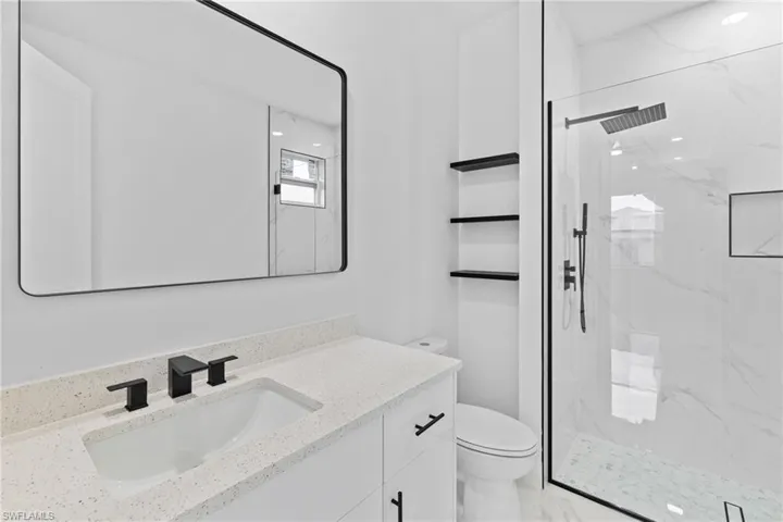 Full bath featuring toilet, vanity, and a marble finish shower