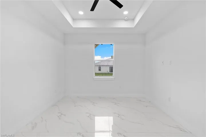 Spare room featuring baseboards, ceiling fan, a tray ceiling, marble finish flooring, and recessed lighting