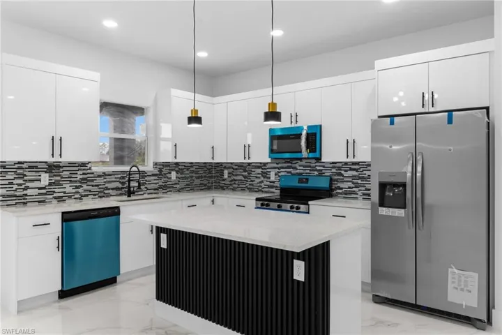 Kitchen with appliances with stainless steel finishes, a sink, light marble finish flooring, white cabinets, and pendant lighting