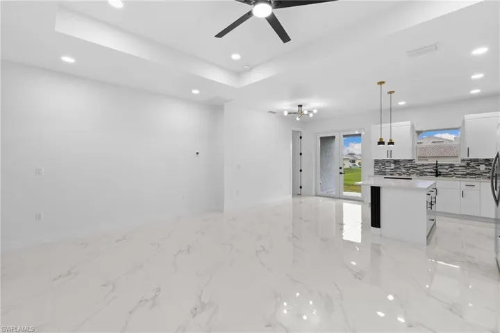 Unfurnished living room with recessed lighting, ceiling fan, a sink, and a tray ceiling