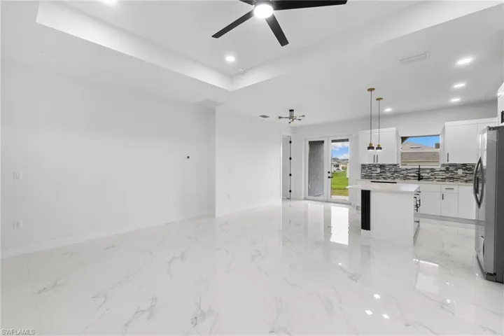 Unfurnished living room featuring a ceiling fan, a sink, baseboards, recessed lighting, and a tray ceiling