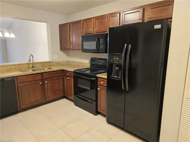 Kitchen with black appliances, a sink, a textured ceiling, light granite countertops, and a chandelier