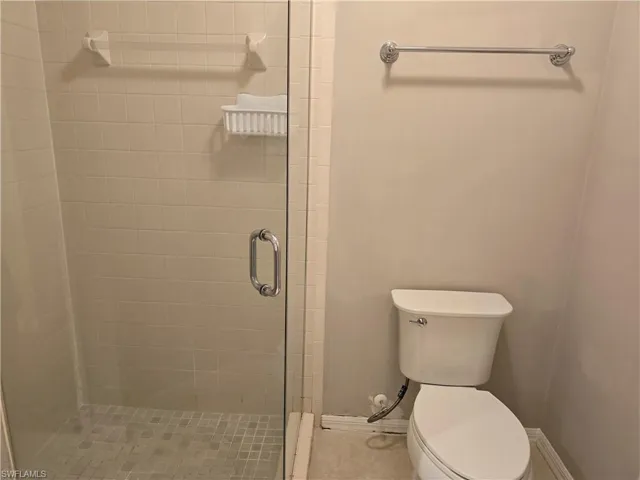 Bathroom featuring a stall shower, toilet, and baseboards
