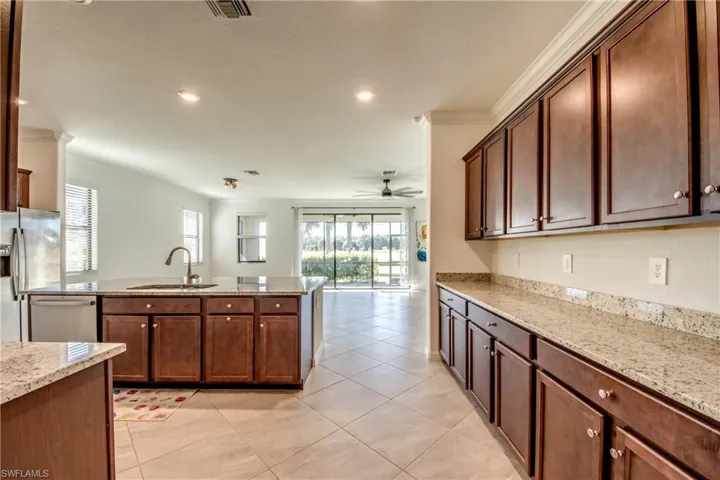 Kitchen featuring light stone countertops, crown molding, light tile patterned floors, stainless steel appliances, and a ceiling fan