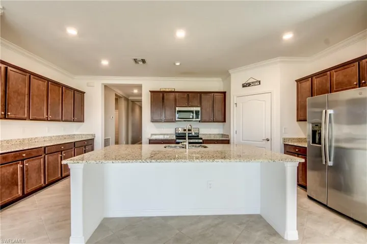 Kitchen featuring appliances with stainless steel finishes, crown molding, a kitchen island with sink, recessed lighting, and light stone countertops
