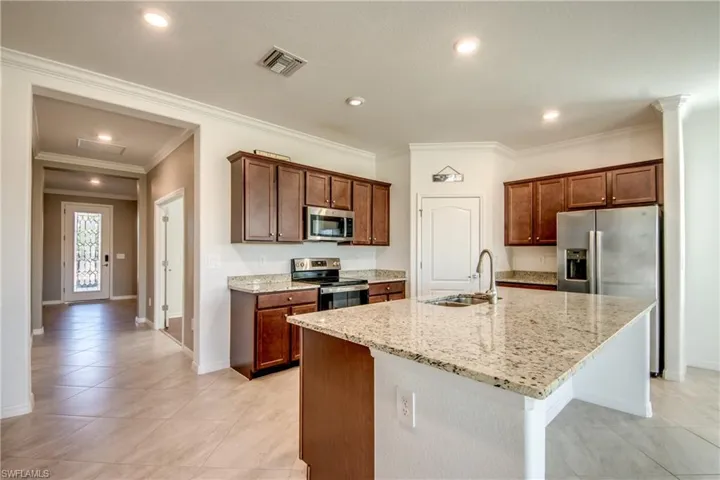 Kitchen featuring appliances with stainless steel finishes, light stone countertops, recessed lighting, ornamental molding, and a center island with sink