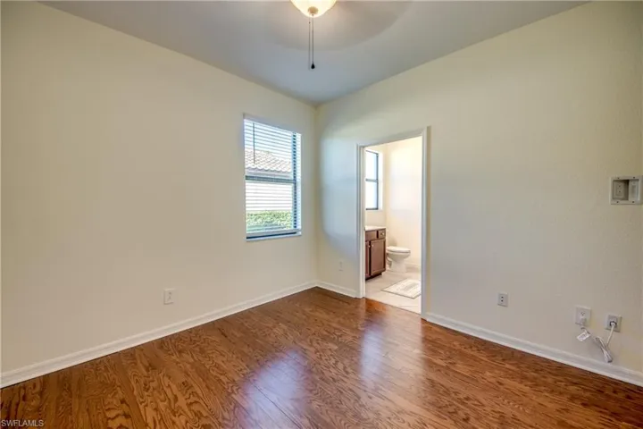 Unfurnished bedroom featuring dark wood-style flooring, a ceiling fan, and connected bathroom