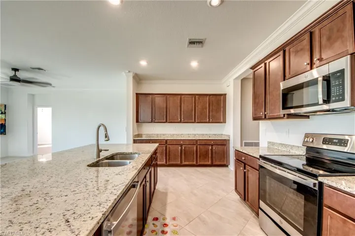Kitchen with stainless steel appliances, crown molding, light tile patterned floors, light stone counters, and a ceiling fan