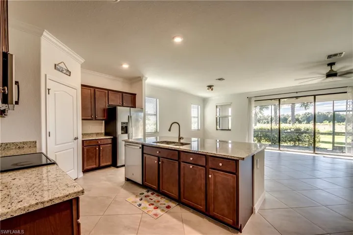 Kitchen with light stone counters, crown molding, an island with sink, light tile patterned floors, and stainless steel appliances