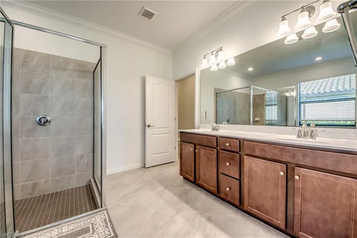 Bathroom featuring double vanity, a stall shower, ornamental molding, and light tile patterned floors